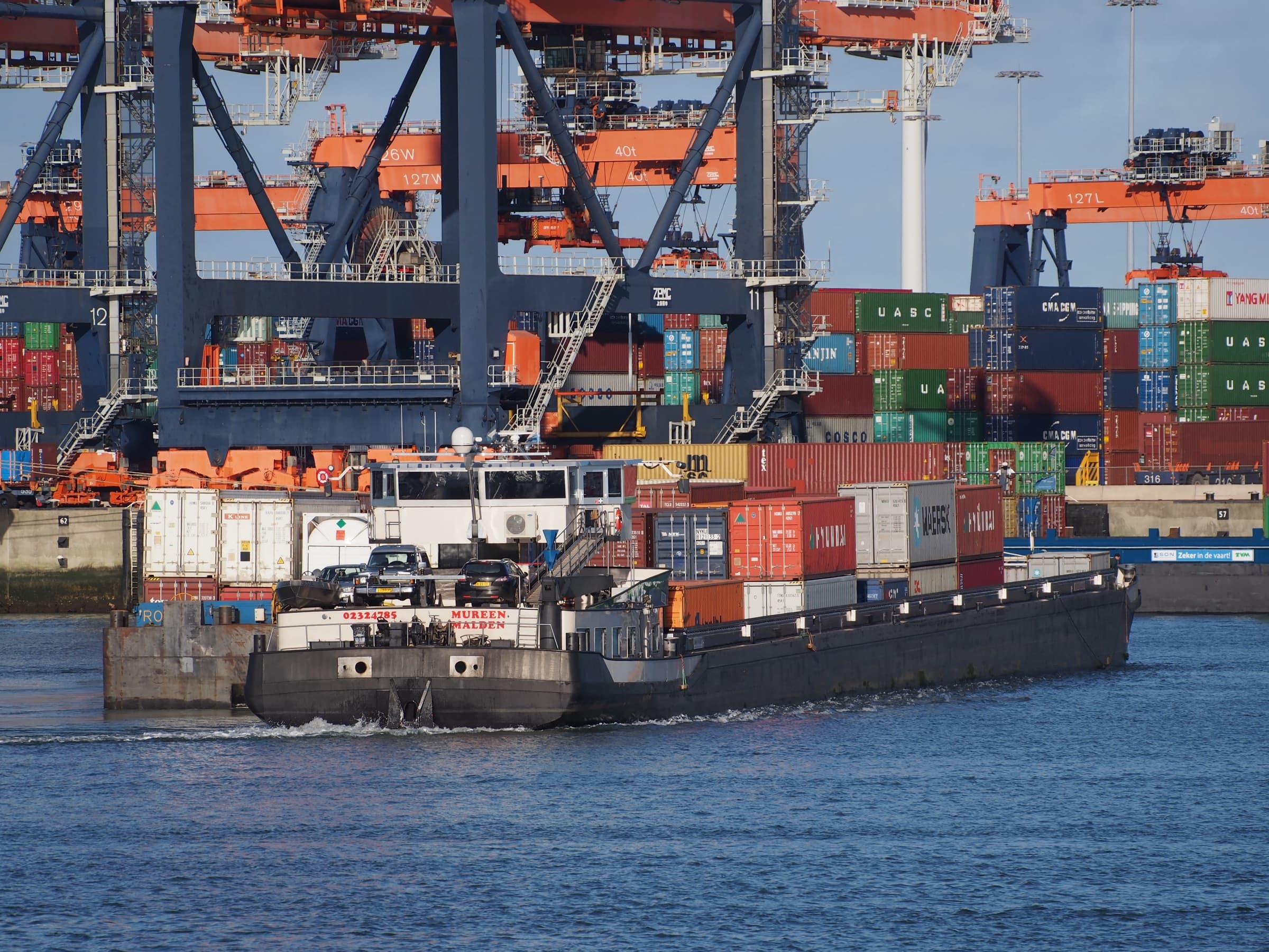 Containerbinnenvaartschip Mureen vaart langs de kranen van een containerterminal in de Rotterdamse haven